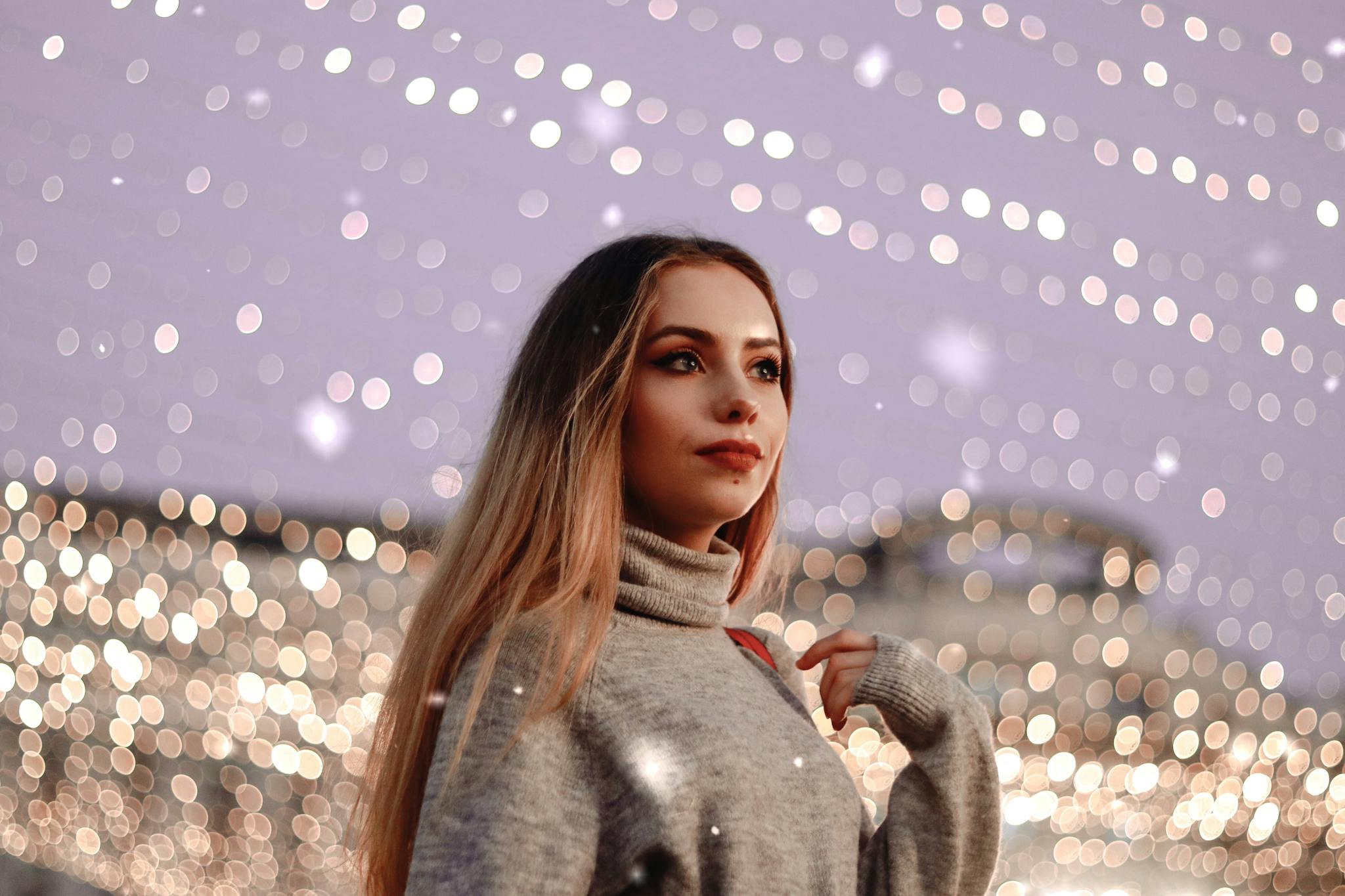 Portrait of stylish woman in cozy sweater with enchanting bokeh lights background.
