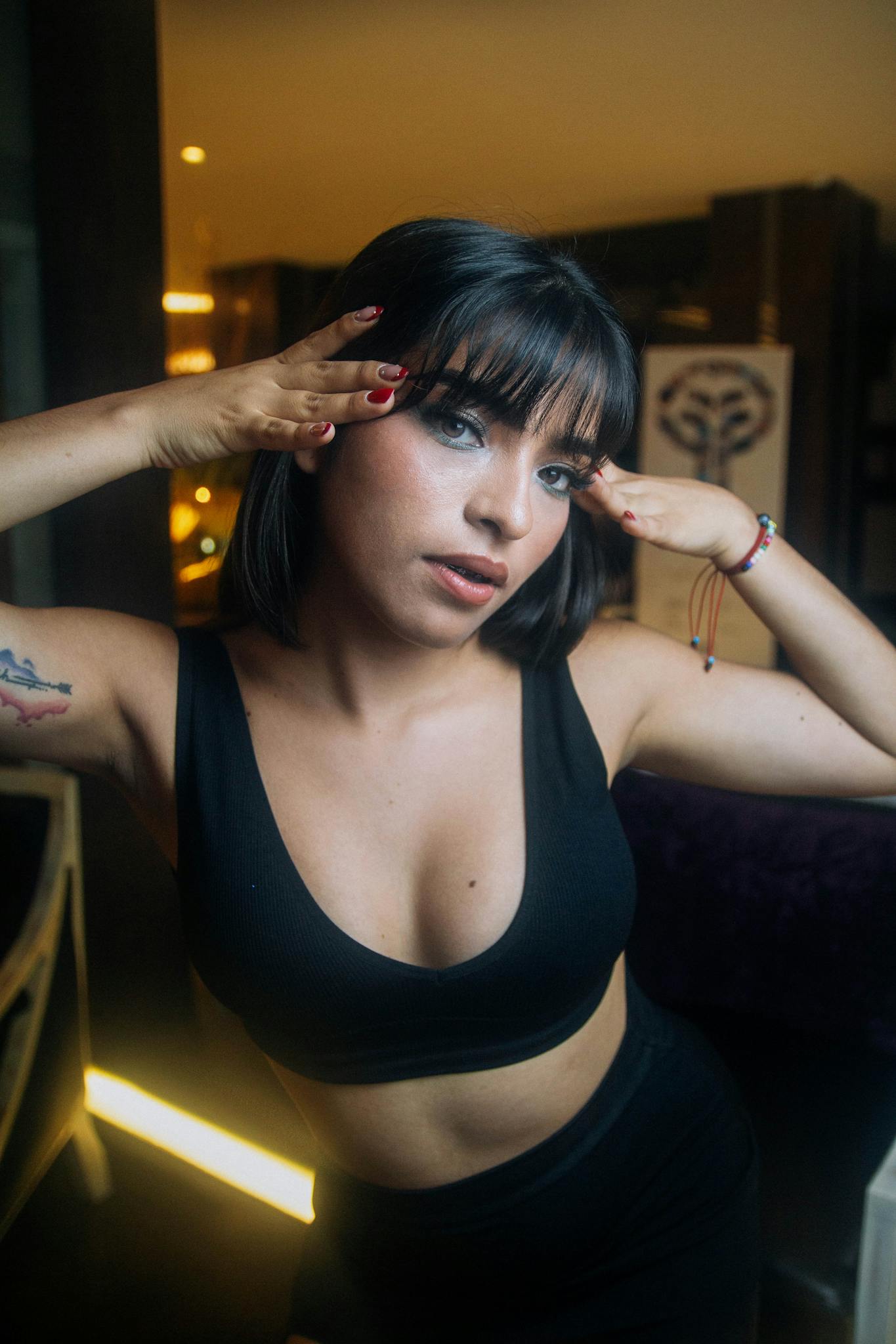 Stylish young woman with tattoos striking a pose indoors, showcasing a trendy look.