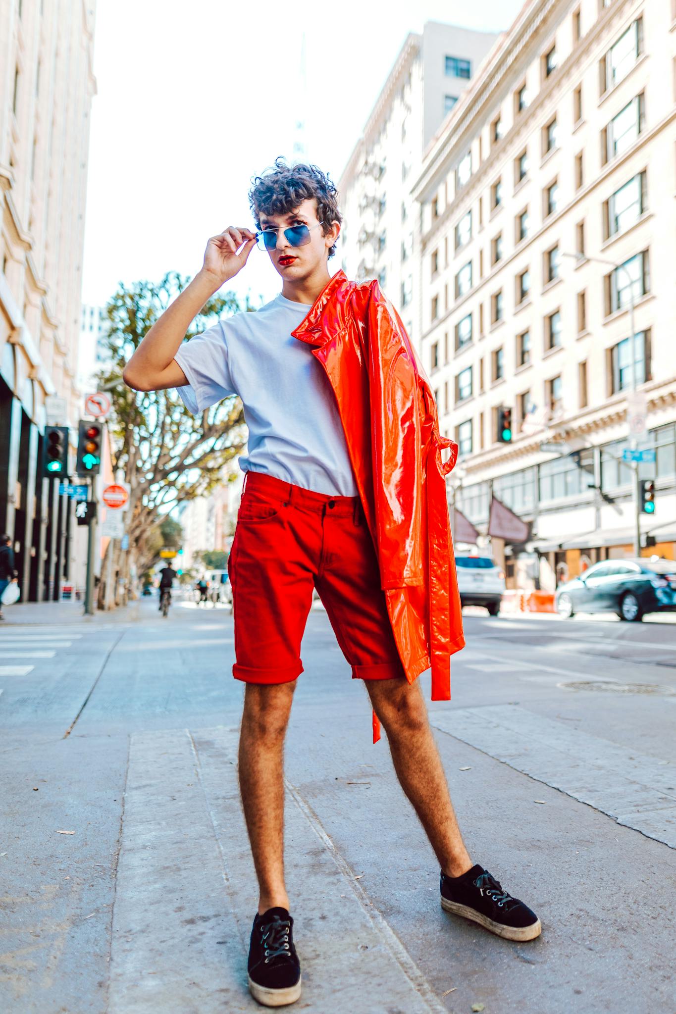 Trendy young adult showcasing vibrant street fashion with a red jacket and sunglasses in a city setting.